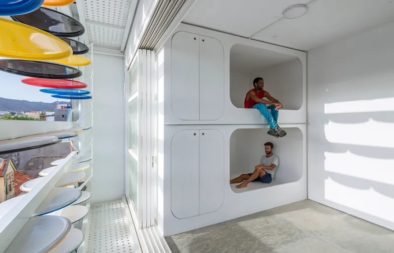 White built-in alcove sleeping niches with two occupants beside shelving displaying colored ceramic plates and bowls