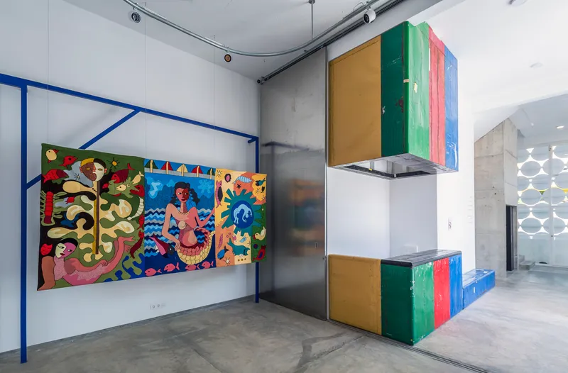 Gallery interior with multicolored striped kitchen volume beside concrete wall and blue steel frame