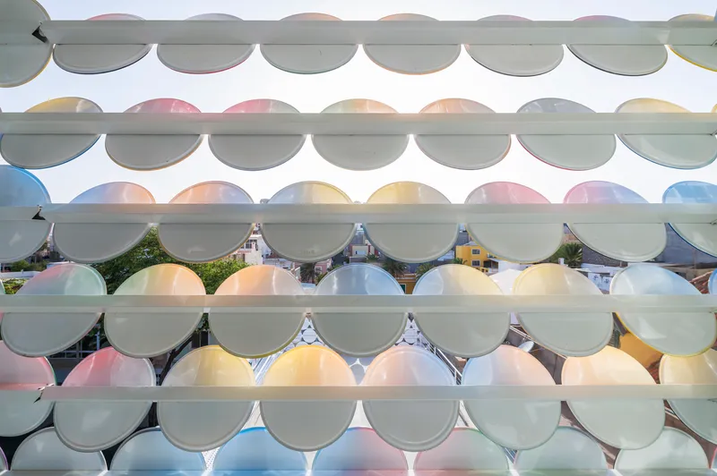 Facade detail showing overlapping translucent circular glass panels in pastel hues on horizontal supports