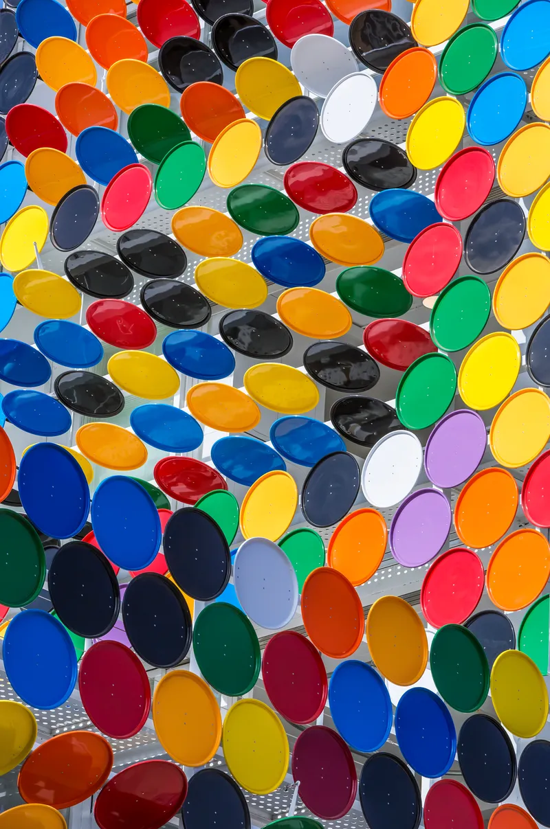 Close-up of multicolored oval glass lenses set in perforated metal screen in bright daylight