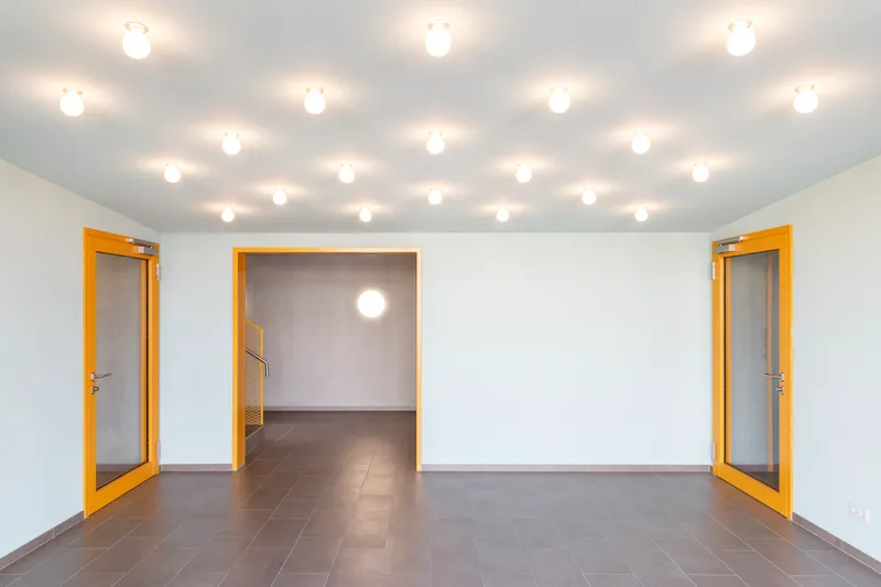 White interior hallway with yellow-trimmed doorways and grid of ceiling-mounted globe fixtures
