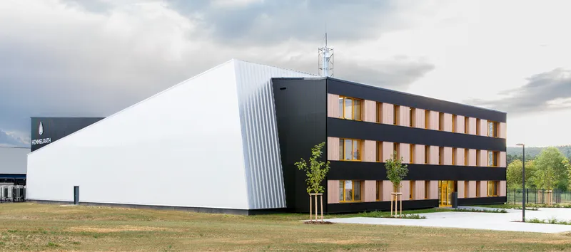 Corner view of white ribbed volume and black office wing with timber-framed windows under cloudy skies