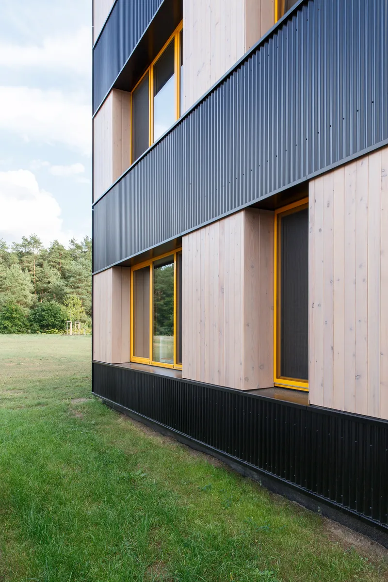 Side elevation showing alternating bands of dark metal cladding and light timber with yellow-framed windows