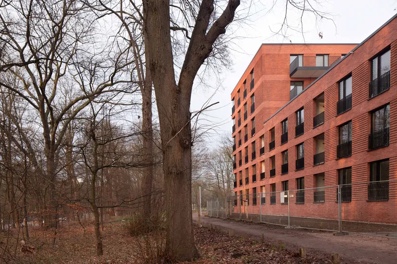 Red brick residential block seen from the adjacent woodland with bare trees in late autumn
