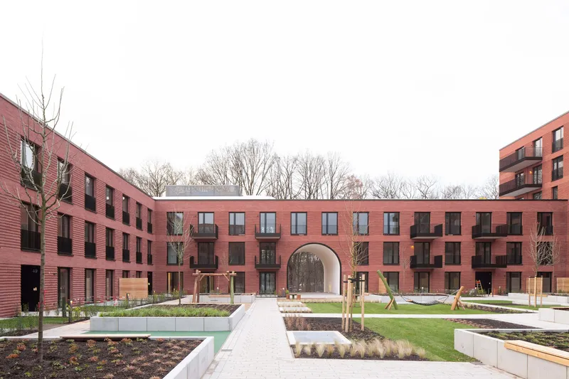 Central courtyard with landscaped beds and paved pathway framed by red brick residential blocks with a central archway