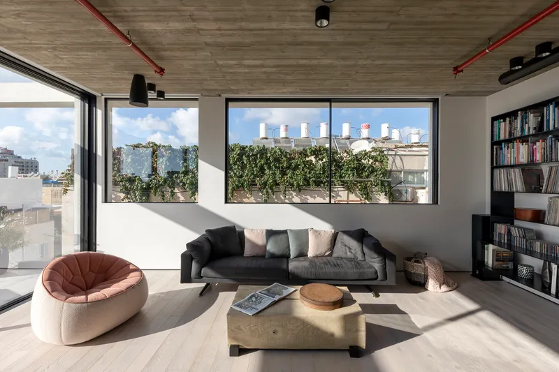Living room with corner glazing overlooking planted terrace under daylight streaming across pale wood flooring