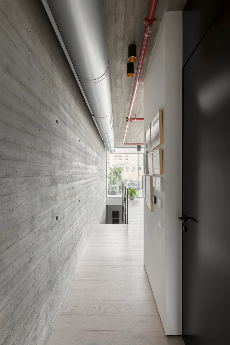 Narrow corridor with board-formed concrete wall alongside exposed HVAC ductwork and red fire suppression piping