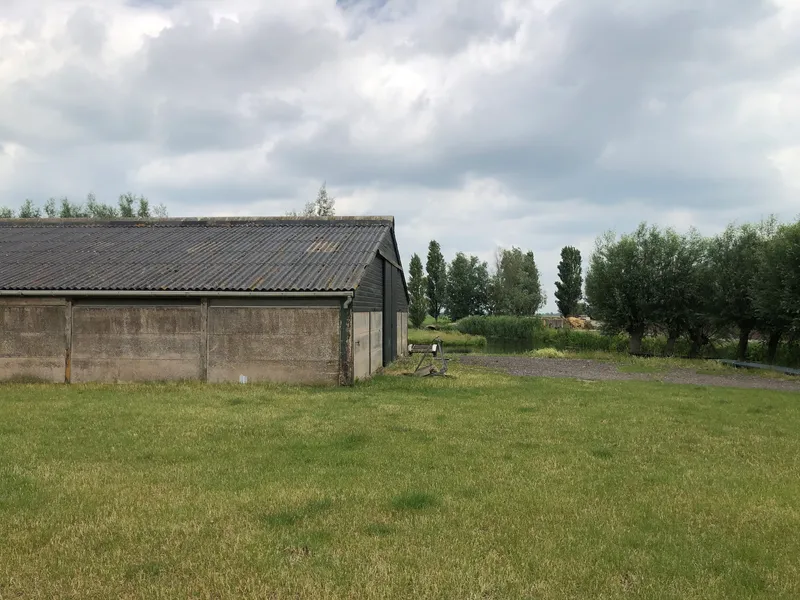 Converted barn with concrete walls and metal roof extension across a grassy field under clouds