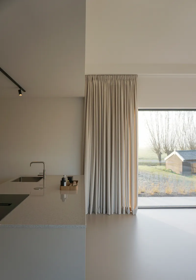 Kitchen island with integrated sink beneath linen curtains and a large window overlooking bare winter trees