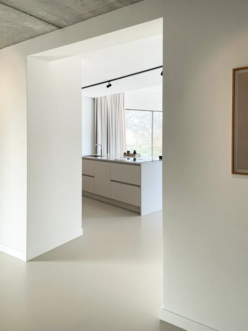 Threshold between rooms with exposed concrete ceiling and pale resin floor