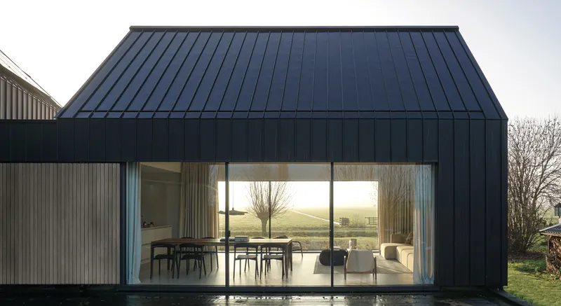 Full-height glazed wall opening onto a terrace with views of pollarded trees and distant fields