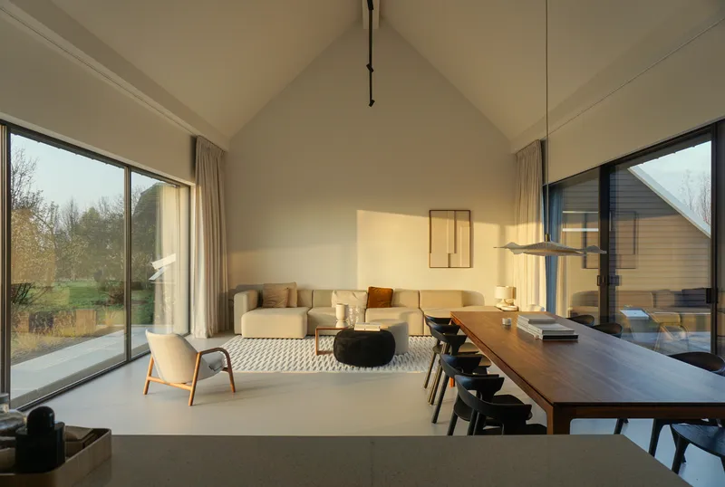 Open-plan living and dining space with vaulted plywood ceiling and corner windows framing bare trees