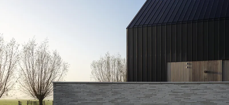 Horizontal stacked stone base wall beneath dark vertical cladding with a tree in misty light