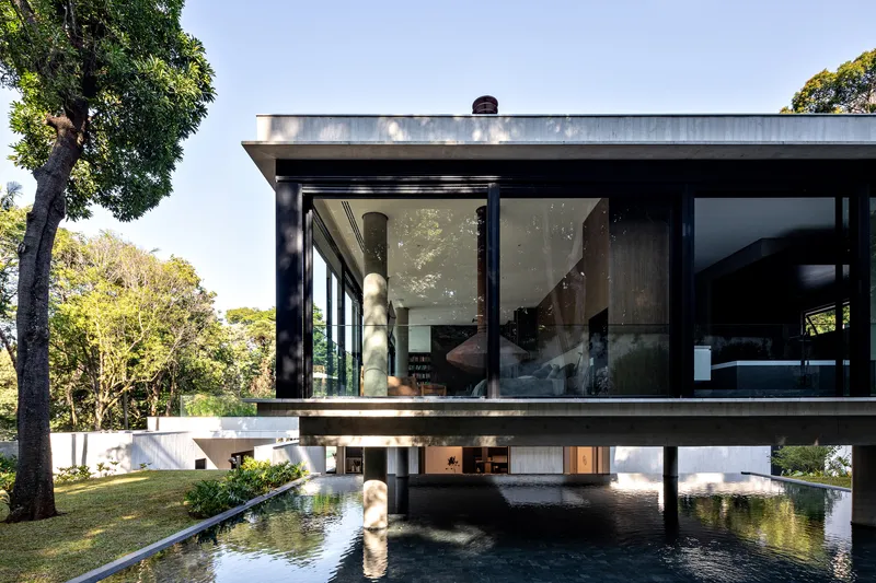 Cantilevered upper floor with floor-to-ceiling windows reflected in the pool below with figure at water's edge