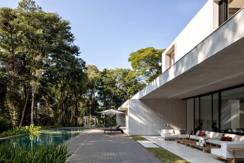 Concrete cantilevered upper floor shading a covered seating area beside a timber deck and reflecting pool