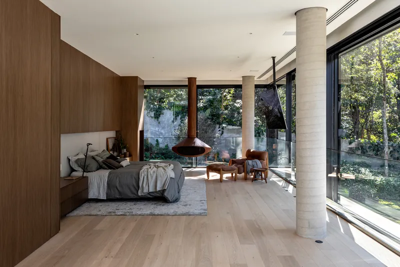 Bedroom with timber millwork and a suspended fireplace facing full-height glazing and a pool