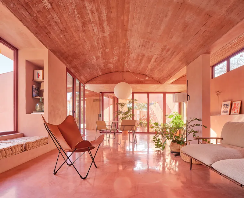 Living room with vaulted timber ceiling, terracotta polished floor and potted plants in warm afternoon light
