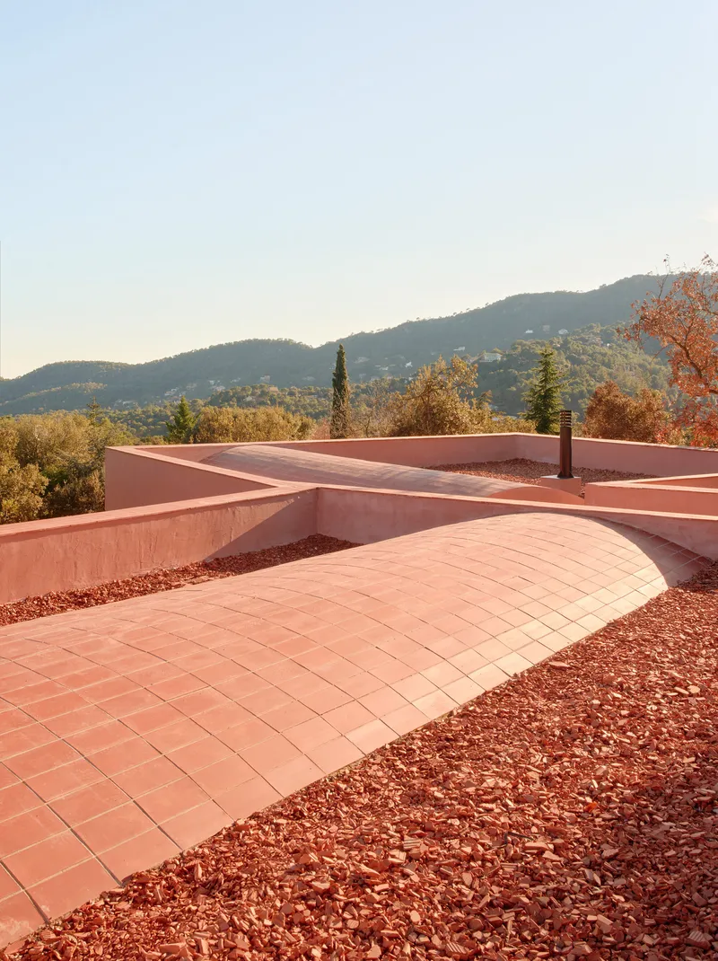 Rooftop terrace with curved tile paving, crushed stone beds and hillside views in morning light