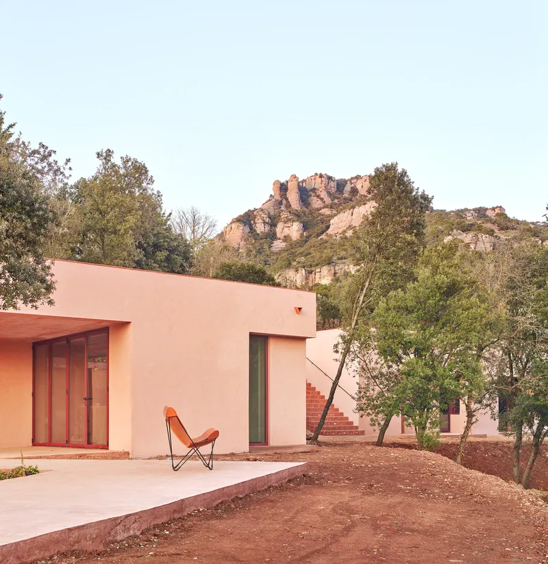 Pink stucco facade with concrete terrace and canvas butterfly chair set against a rocky hillside