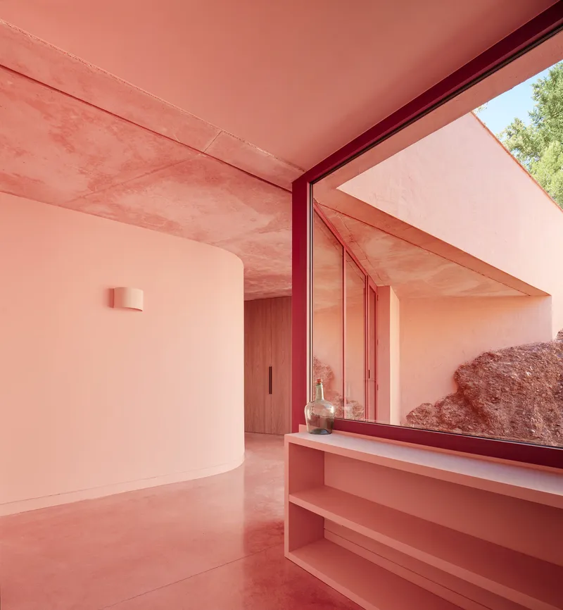 Interior passage with built-in shelving, red steel window frame, and exposed rock outcrop visible outside