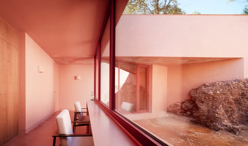 Bench seating along glazed wall overlooking a sunlit courtyard with red earth and exposed rock