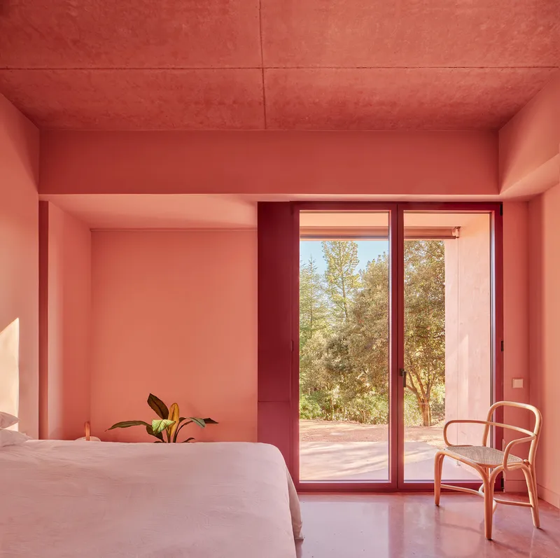 Bedroom with pink stucco walls, sliding glass doors to garden, and bentwood chair beside the bed