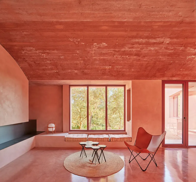 Living room with vaulted timber ceiling, triptych window framing trees, and pink concrete floors
