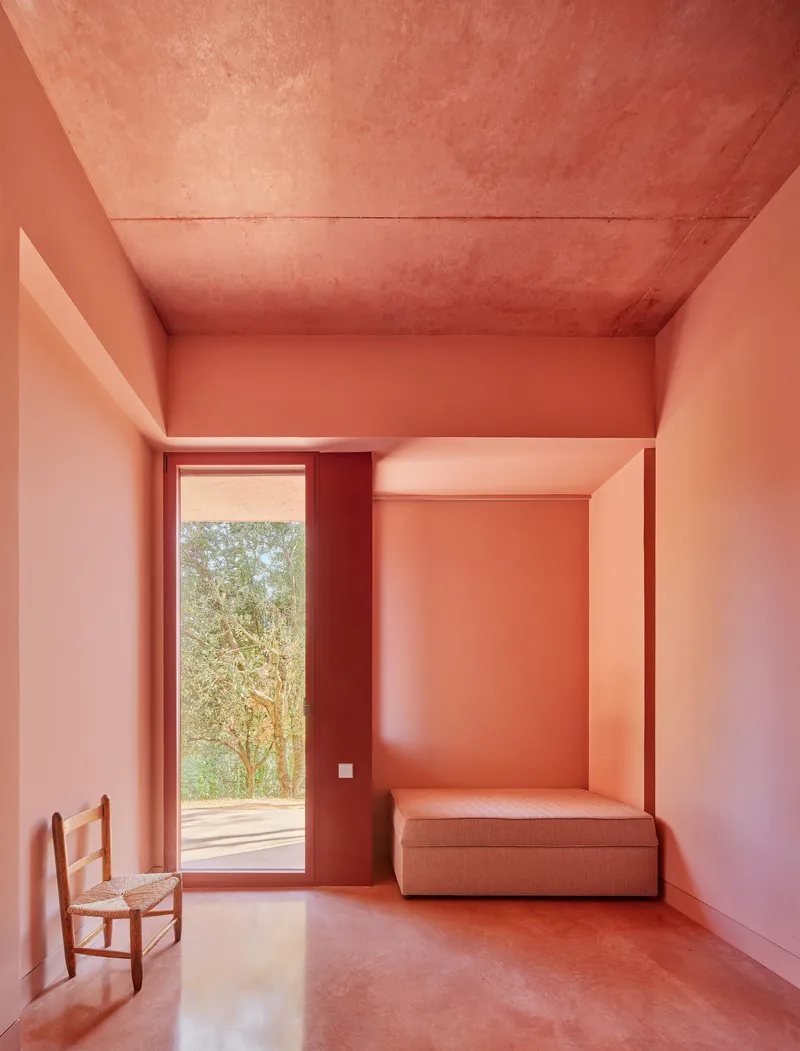 Bedroom with tall window framing trees outside and built-in bed niche in pink plaster