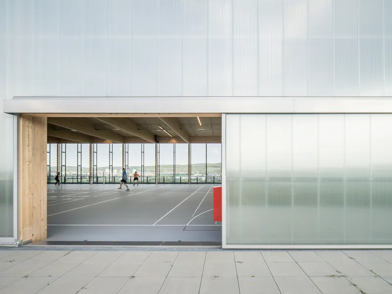 Open sliding translucent panel revealing the sports court interior framed by timber structure