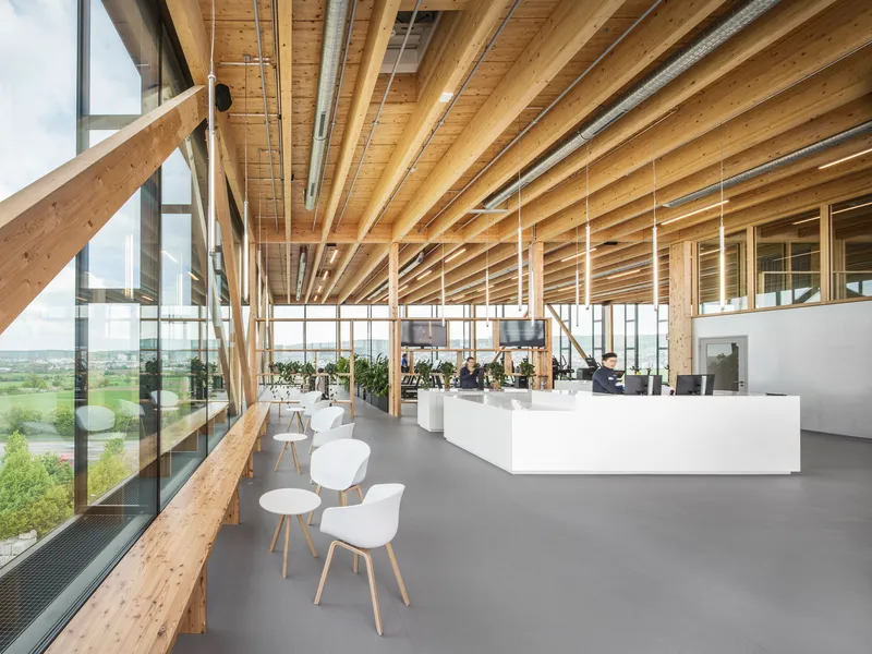 Open plan office space with exposed timber beam ceiling and full-height glazing overlooking green fields