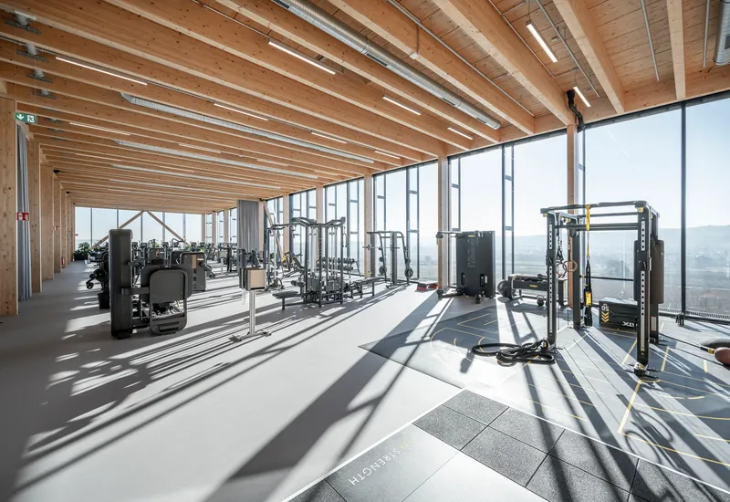 Fitness area with gym equipment beneath timber joists casting long shadows across the floor