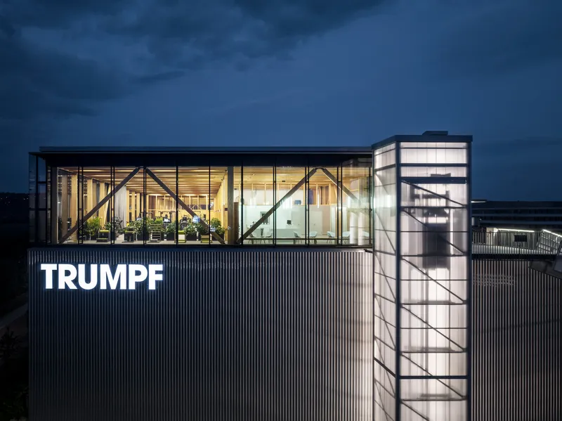 Rooftop glazed pavilion with exposed diagonal bracing and cylindrical stair tower at twilight