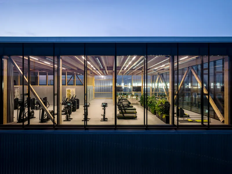 Exterior view through floor-to-ceiling windows revealing gym equipment and planted pots at dusk