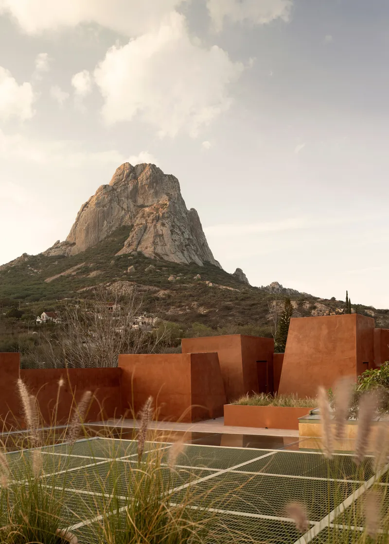 Red stucco volumes with tennis court and rocky mountain peak in the background