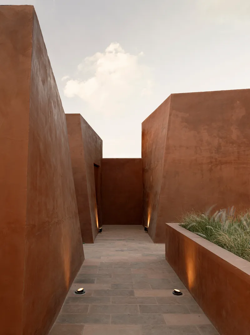 Passageway between corten steel walls with planted bed and uplighting beneath a white cloud-filled sky