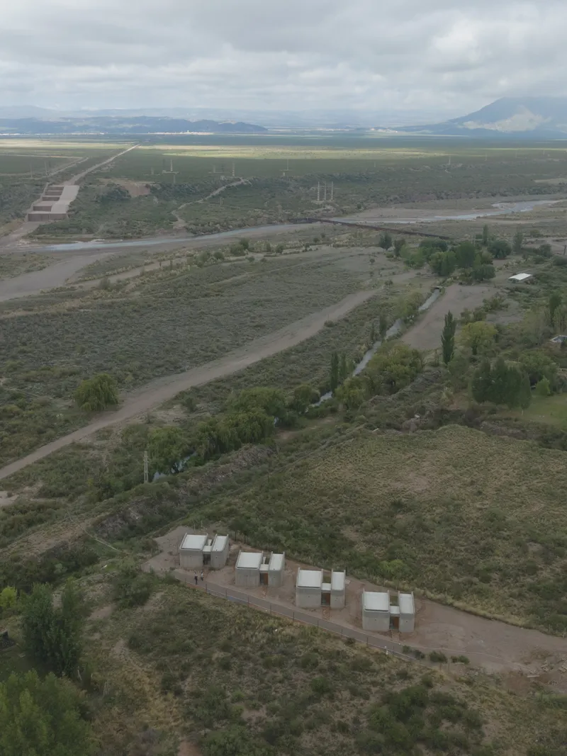 Oblique aerial view of four paired white housing units along a road with distant mountains and cloudy sky