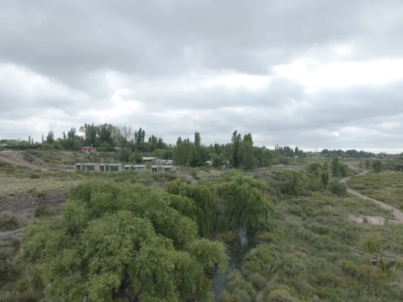 Distant view of low white housing structures set among trees and scrubland under heavy grey clouds
