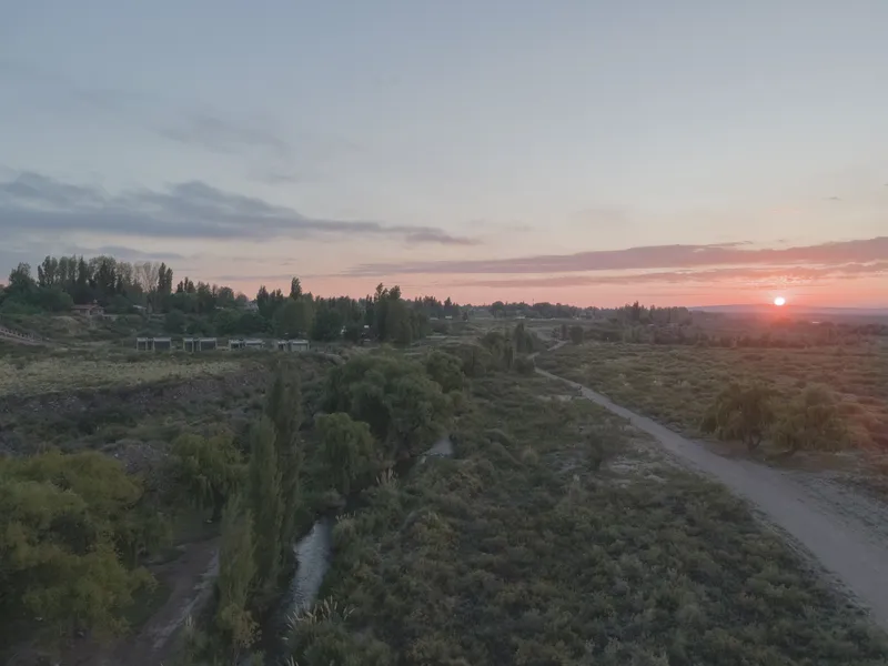 Wide landscape view showing irrigation canal bordered by poplars and scrubland at sunset