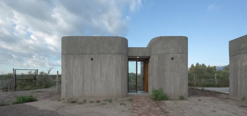 Entry facade with twin cylindrical concrete volumes flanking a glazed door at twilight