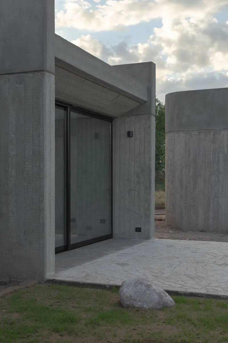 Recessed glass door beneath a concrete canopy flanked by cylindrical concrete volumes