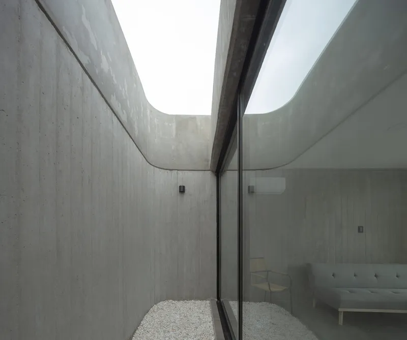Narrow gravel courtyard between curved concrete walls with a clerestory opening above