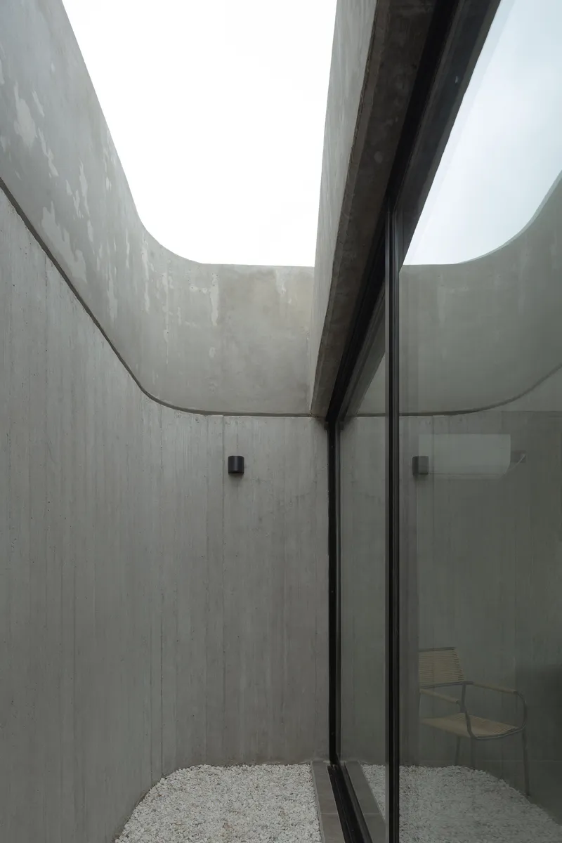 Board-formed concrete courtyard with curved walls and a glazed door under an overcast sky