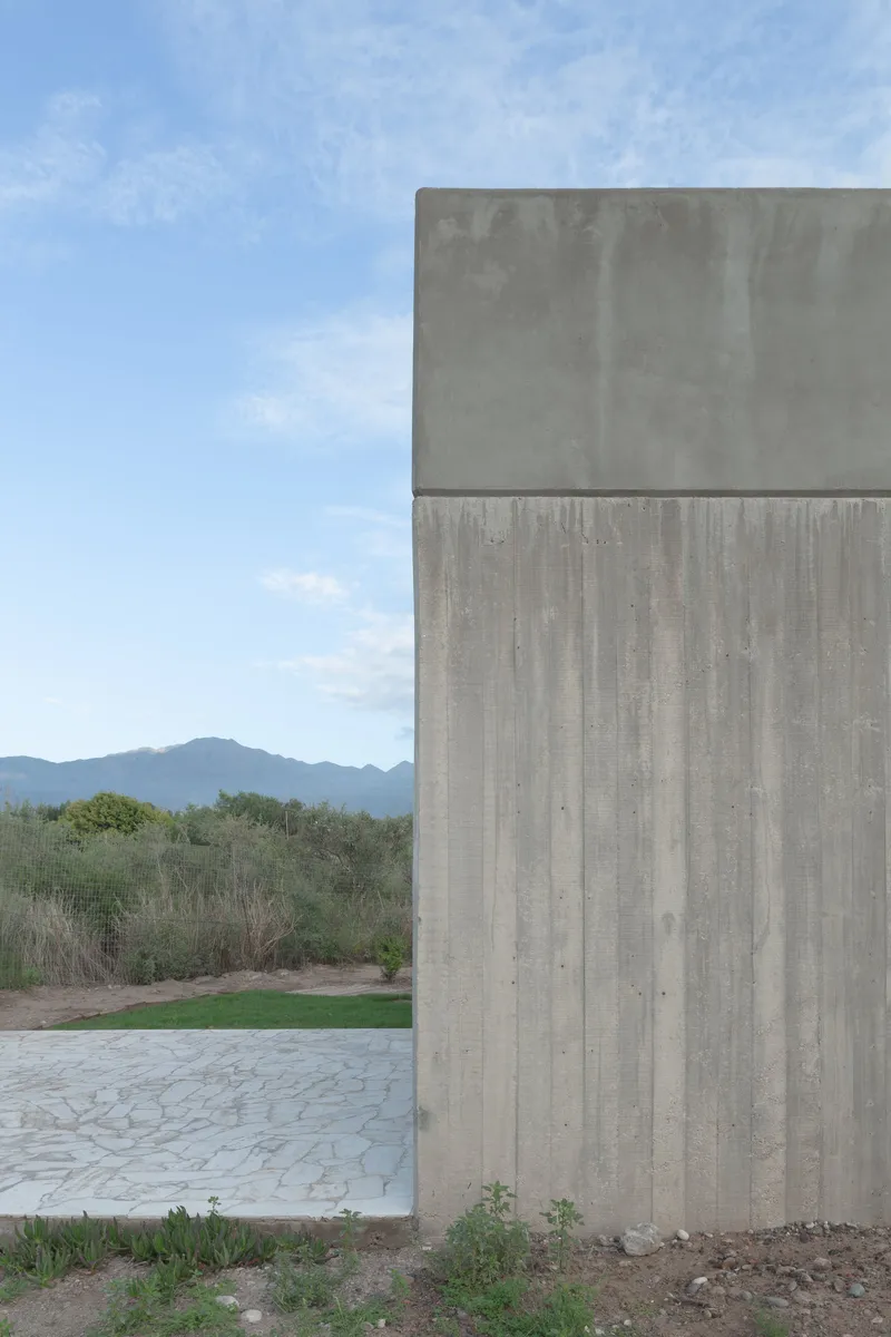 Two-story concrete tower with board formwork texture against mountains and blue sky