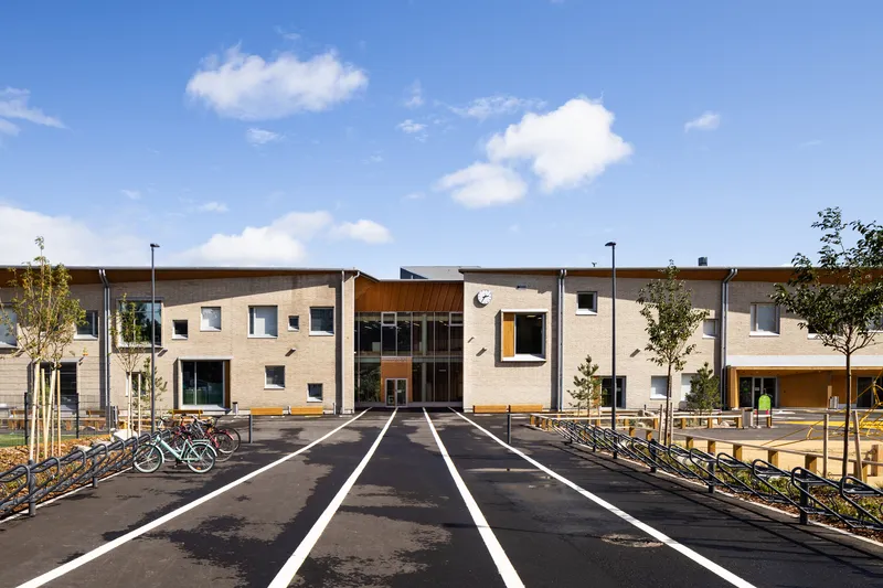 Frontal view of the entrance courtyard with cream brick facades and timber cladding under a blue sky