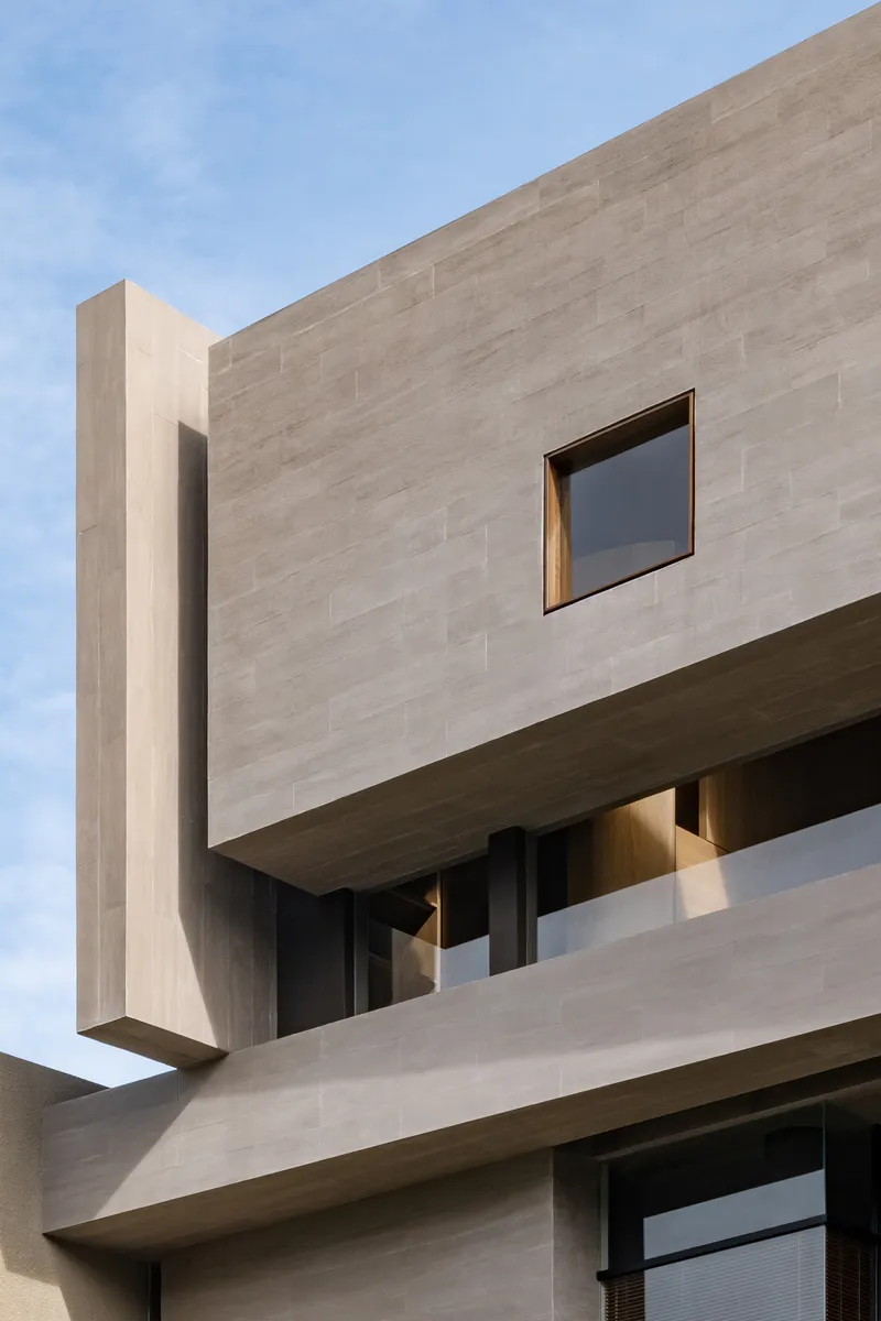 Corner detail of cantilevered concrete volume with square window and timber-lined soffit below