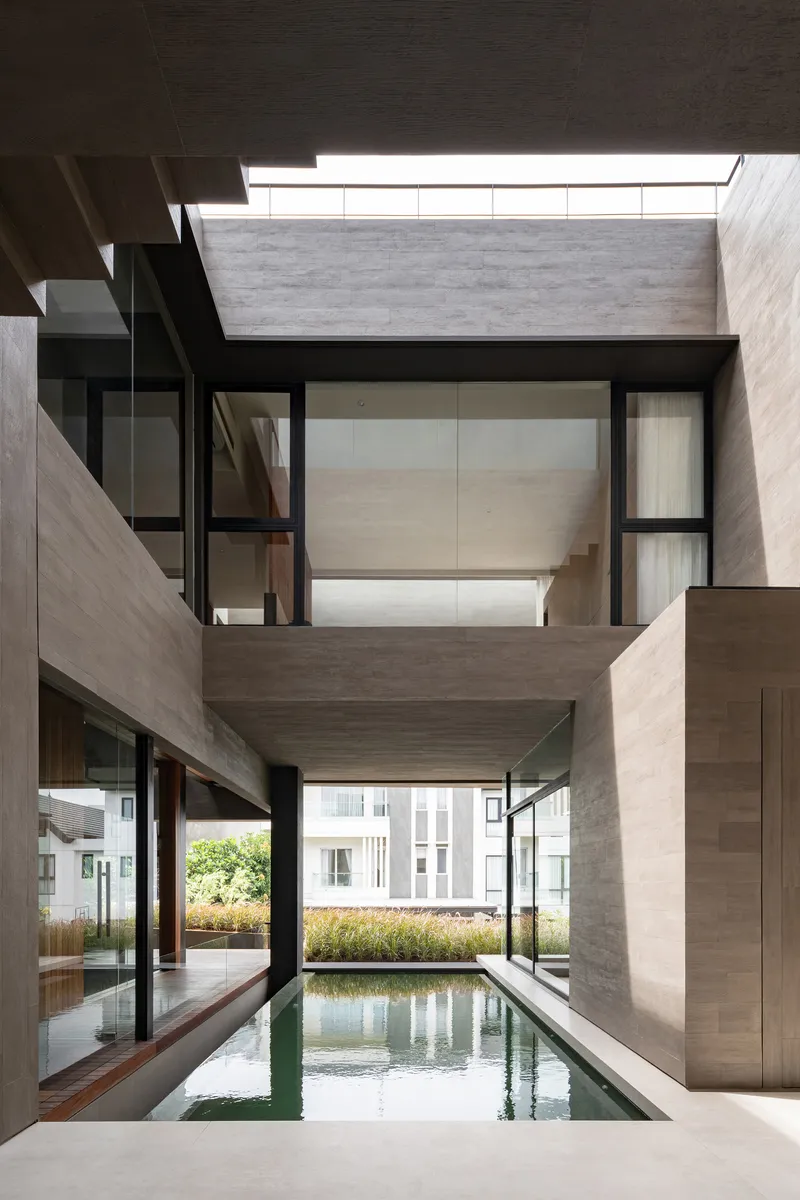 Double-height void with reflecting pool below and glazed bridge crossing between travertine-clad walls