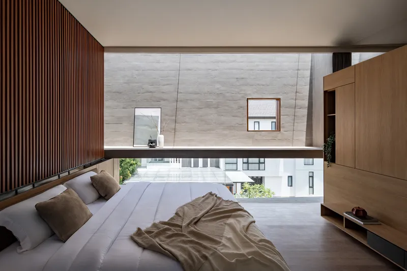 Upper-level bedroom with slatted timber wall and horizontal window overlooking neighboring rooftops and greenery