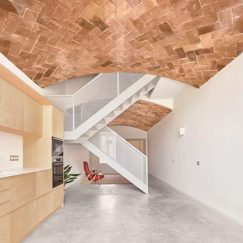 Open living space with herringbone brick vault ceiling, light wood kitchen and white steel staircase