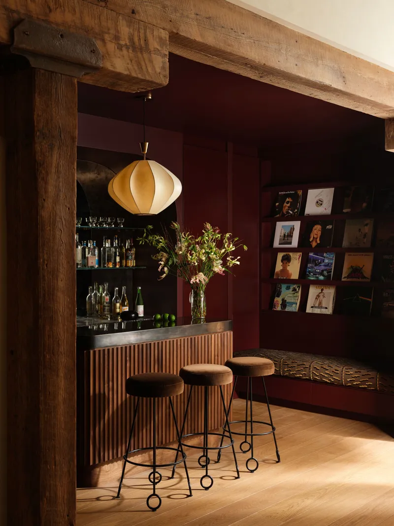Bar nook with fluted timber front, burgundy walls, record display, and pendant light under timber beam