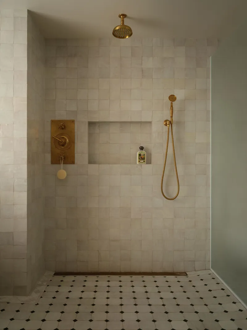 Tiled shower enclosure with brass fixtures and recessed niche on floor with octagonal mosaic pattern